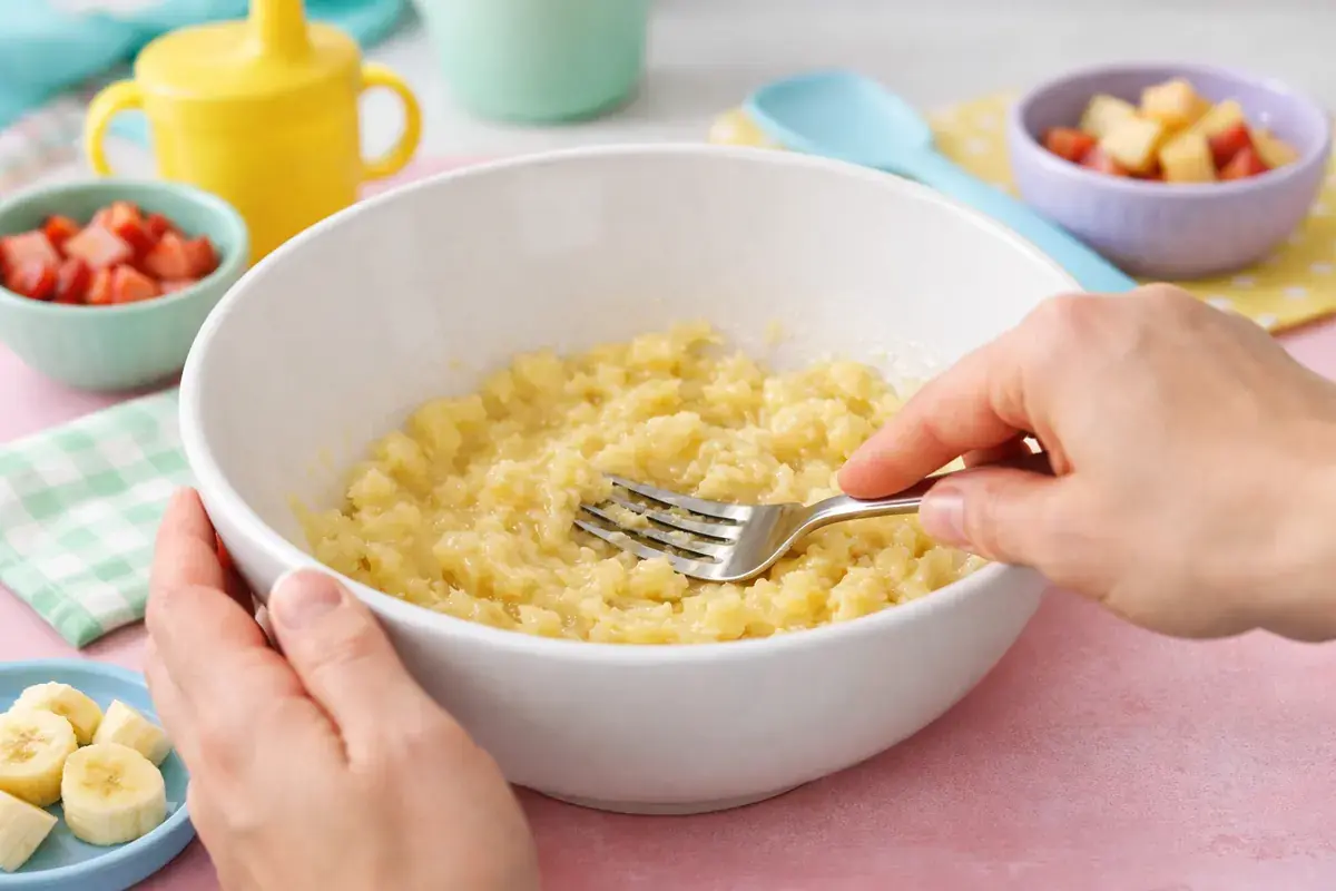 Step 2: A ripe banana being mashed until smooth with a fork in a large mixing bowl